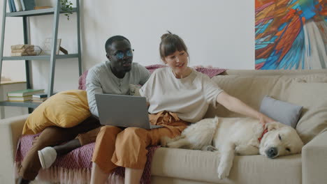 Multiethnic-Couple-Petting-Cute-Dog-on-Sofa-in-Living-Room